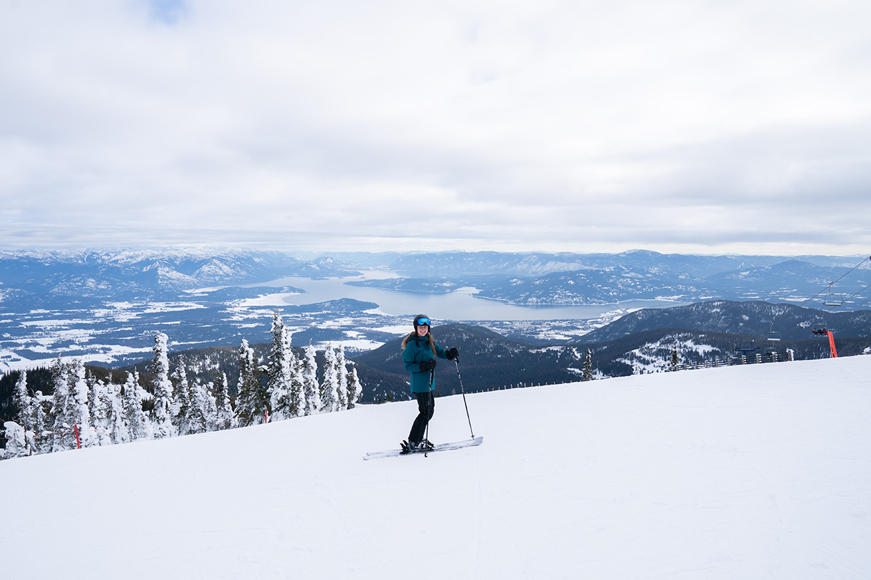 Woman is skiing at Schweitzer mountain with a blue ski jacket on overlooking a lake
