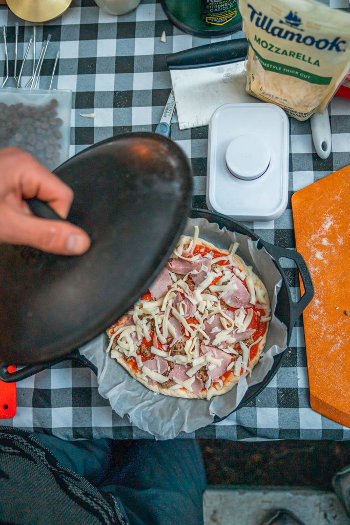 Man is putting lid on cast iron with pizza inside.