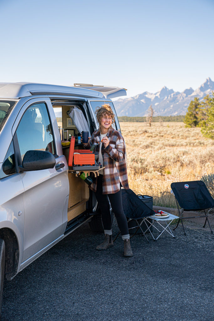 Woman is cooking on an outdoor kitchen setup on a van in grand teton national park.